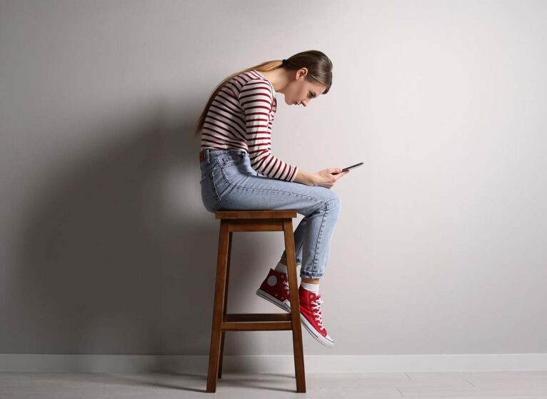 Girl bent over looking at phone while sitting on stool