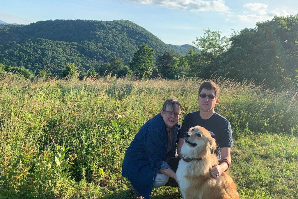 Stage 4 cancer survivor Anne with her husband and dog on their yard near the mountains