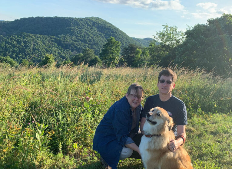 Stage 4 cancer survivor Anne with her husband and dog on their yard near the mountains