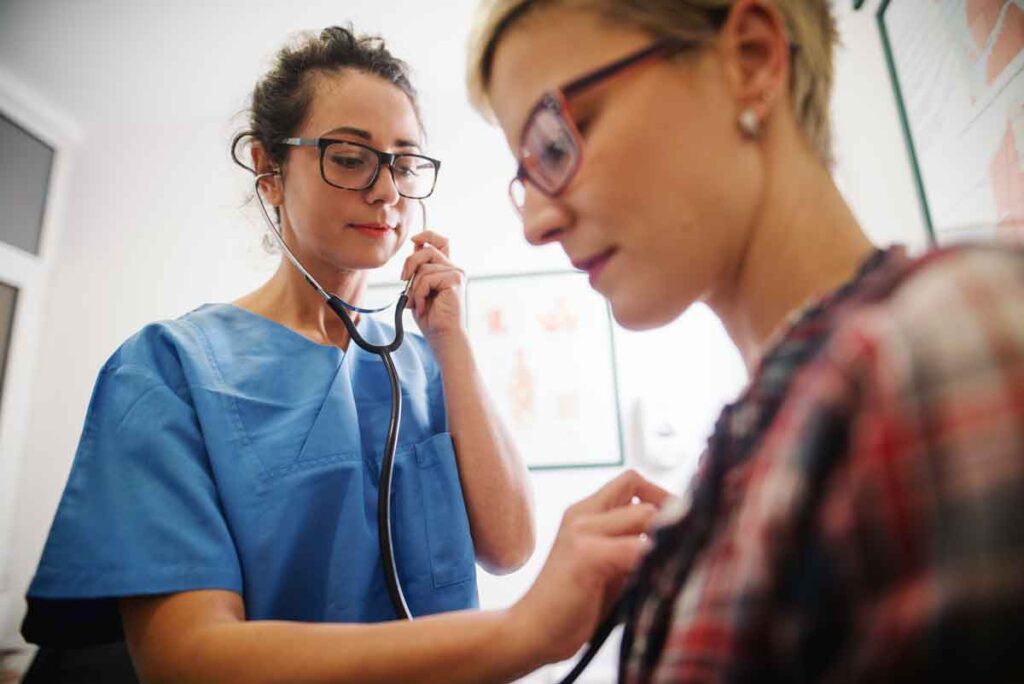 A healthcare provider holding a stethoscope to a woman's chest