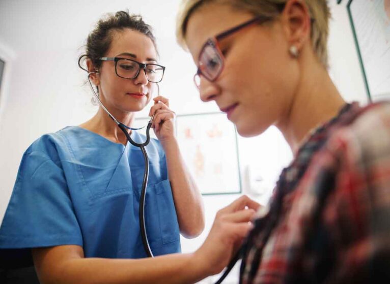 A healthcare provider holding a stethoscope to a woman's chest