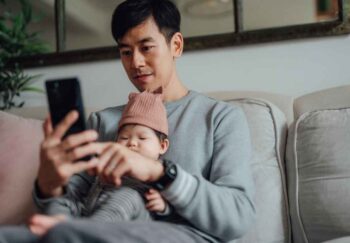 A man sitting while holding a baby and looking at his phone