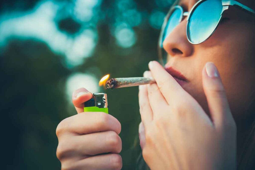 A woman smoking marijuana in a joint, holding a lighter, and wearing sunglasses.