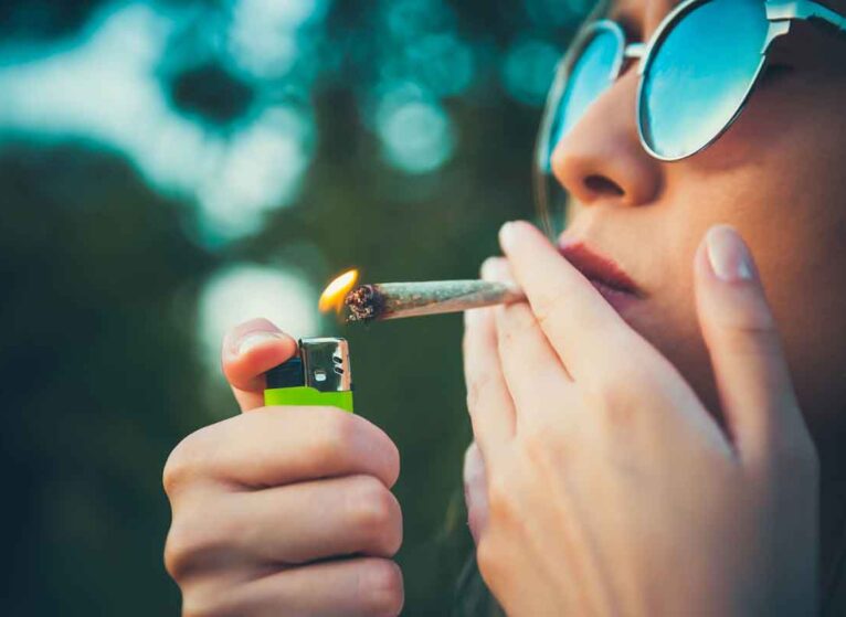 A woman smoking marijuana in a joint, holding a lighter, and wearing sunglasses.