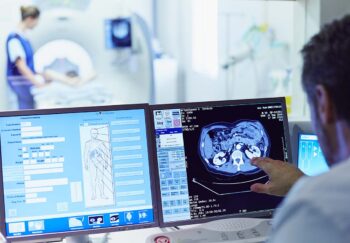 A tech runs a CT scan from control room