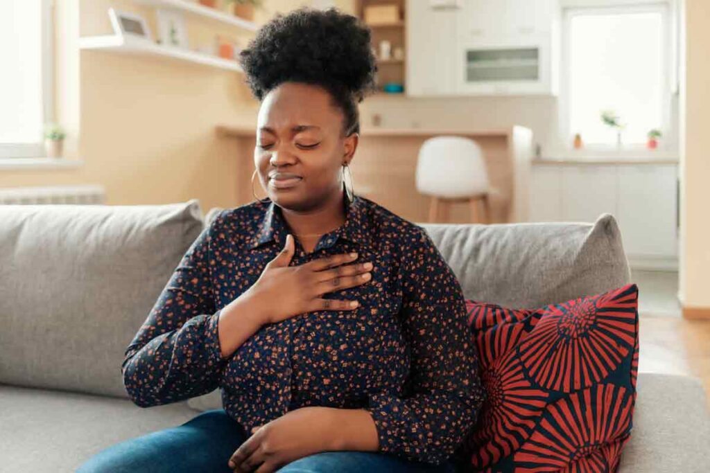 How does Marfan syndrome affect the heart? A woman sitting on a couch with her hand on her chest. She looks in distress.