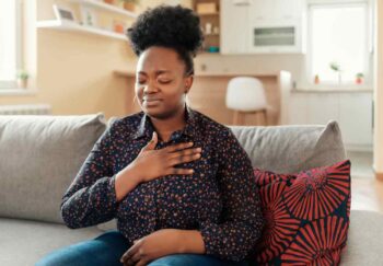 How does Marfan syndrome affect the heart? A woman sitting on a couch with her hand on her chest. She looks in distress.