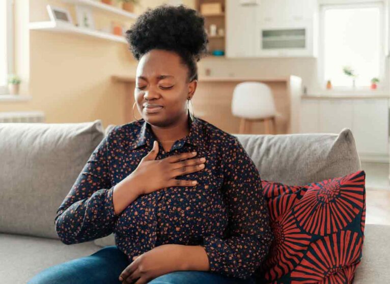 How does Marfan syndrome affect the heart? A woman sitting on a couch with her hand on her chest. She looks in distress.