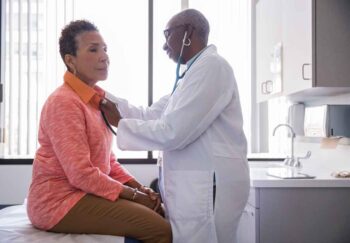 A woman doctor checking the heart of a patient with a stethoscope.