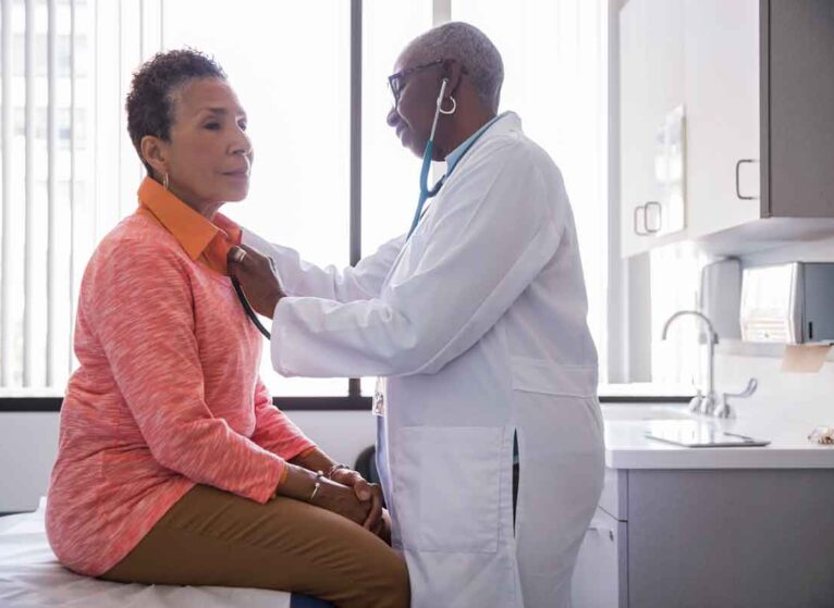 A woman doctor checking the heart of a patient with a stethoscope.