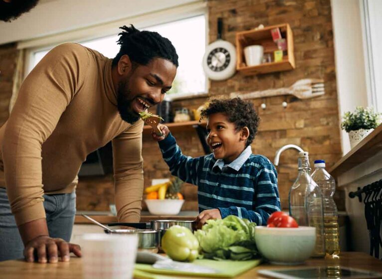 A young boy feeding heart healthy food to his father on a utensil