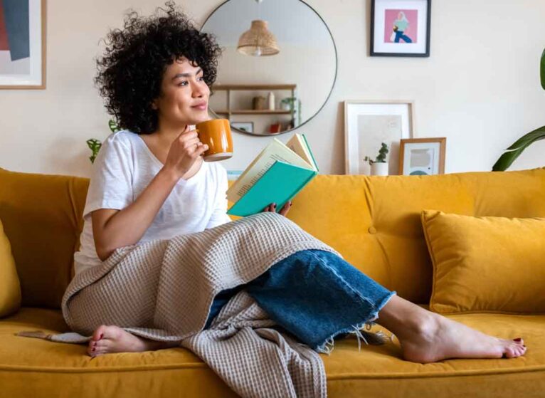 A woman with dark curly hair holding a cup of coffee and looking to the right