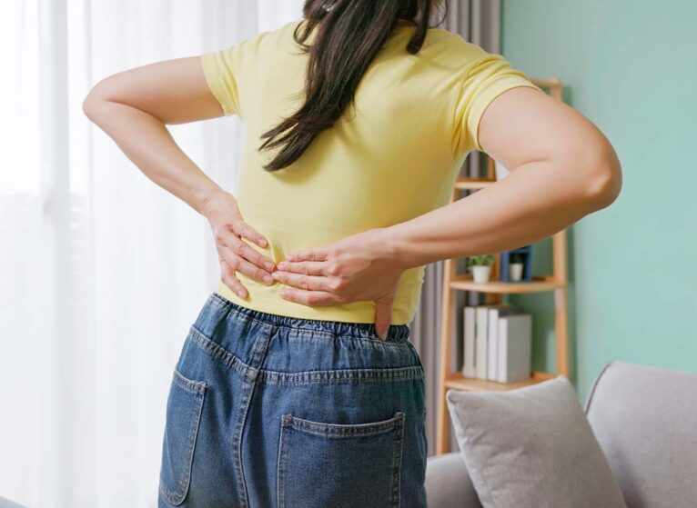 close up woman feels lower back pain in living room at home