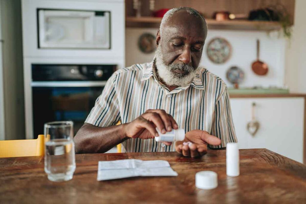 A man sitting at a table looking at a bottle of coronary artery disease medications