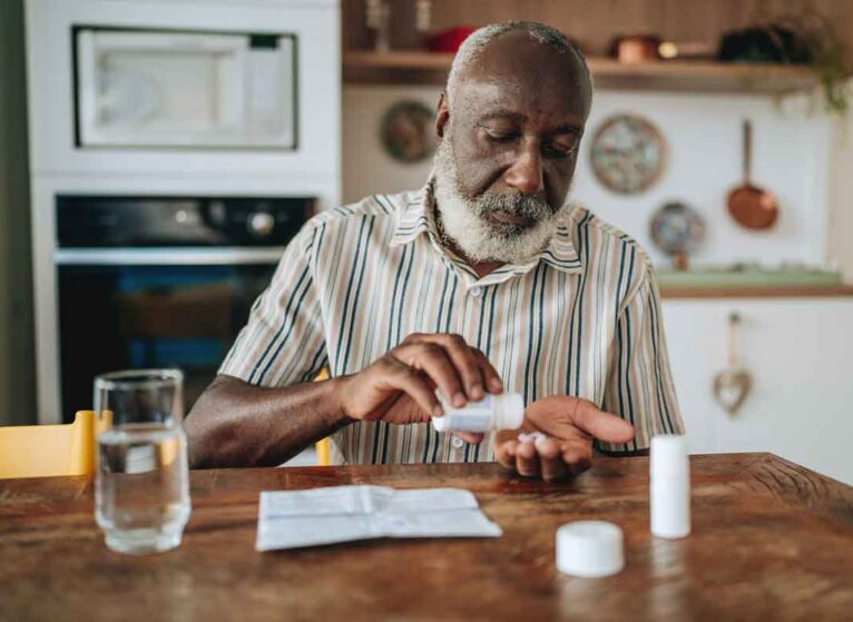 A man sitting at a table looking at a bottle of coronary artery disease medications