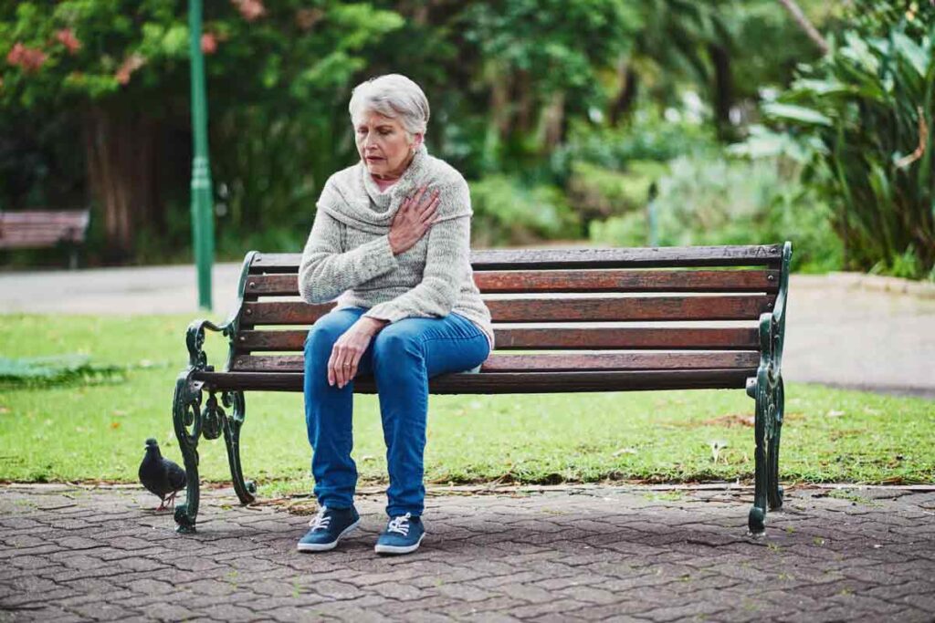 A woman sitting on a park bench and holding her hand over her heart