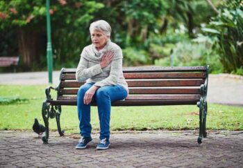 A woman sitting on a park bench and holding her hand over her heart