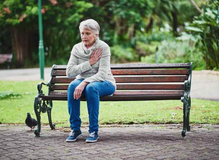 A woman sitting on a park bench and holding her hand over her heart