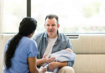 A father sitting on a couch talking to a healthcare provider about circumcision