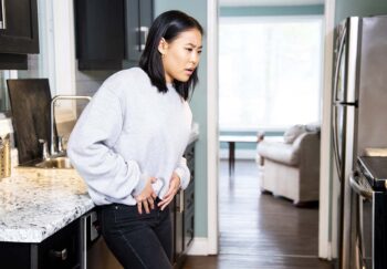 A woman holding her abdominal region in pain standing in her kitchen