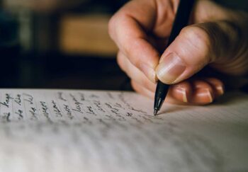 A hand holding a pen and writing on paper