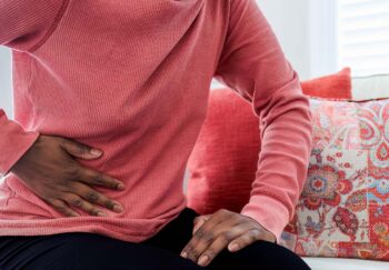 Woman Sits on Couch With Abdominal Pain