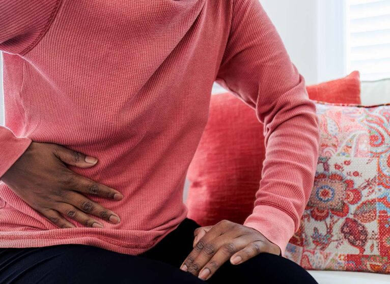 Woman Sits on Couch With Abdominal Pain